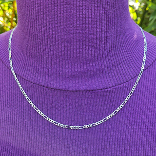 Close-up detail of sterling silver flat Figaro chain links on neck.
