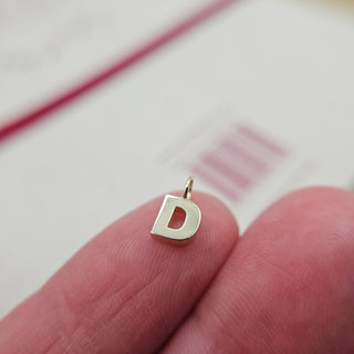 tiny letter D charm on finger for scale in gold