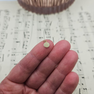 gold disc charm in hand for scale