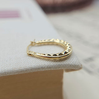 close up of patterned detail on gold creole earrings