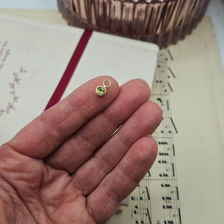 tiny peridot charm in hand for scale