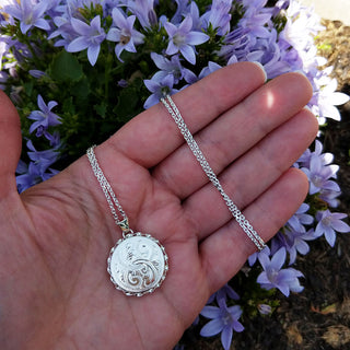 silver locket necklace in hand for scale